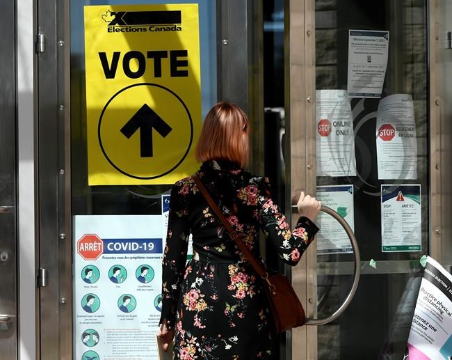 A person passes posters advising measures against COVID-19 as they enter Ottawa City Hall, a polling location, on election day during the 44th Canadian general election, on Monday, Sept. 20, 2021. The Liberals and New Democrats have been declared the winners in two hotly contested British Columbia federal ridings too close to call on election night. THE CANADIAN PRESS/Justin Tang