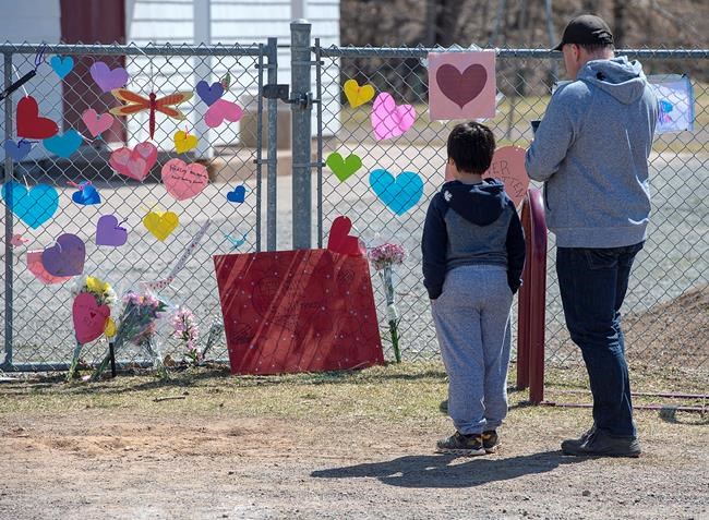 A man and his son pay repects at a memorial to Lisa McCully, a teacher at Debert Elementary School in Debert, N.S. on Tuesday, April 21, 2020. THE CANADIAN PRESS/Andrew Vaughan