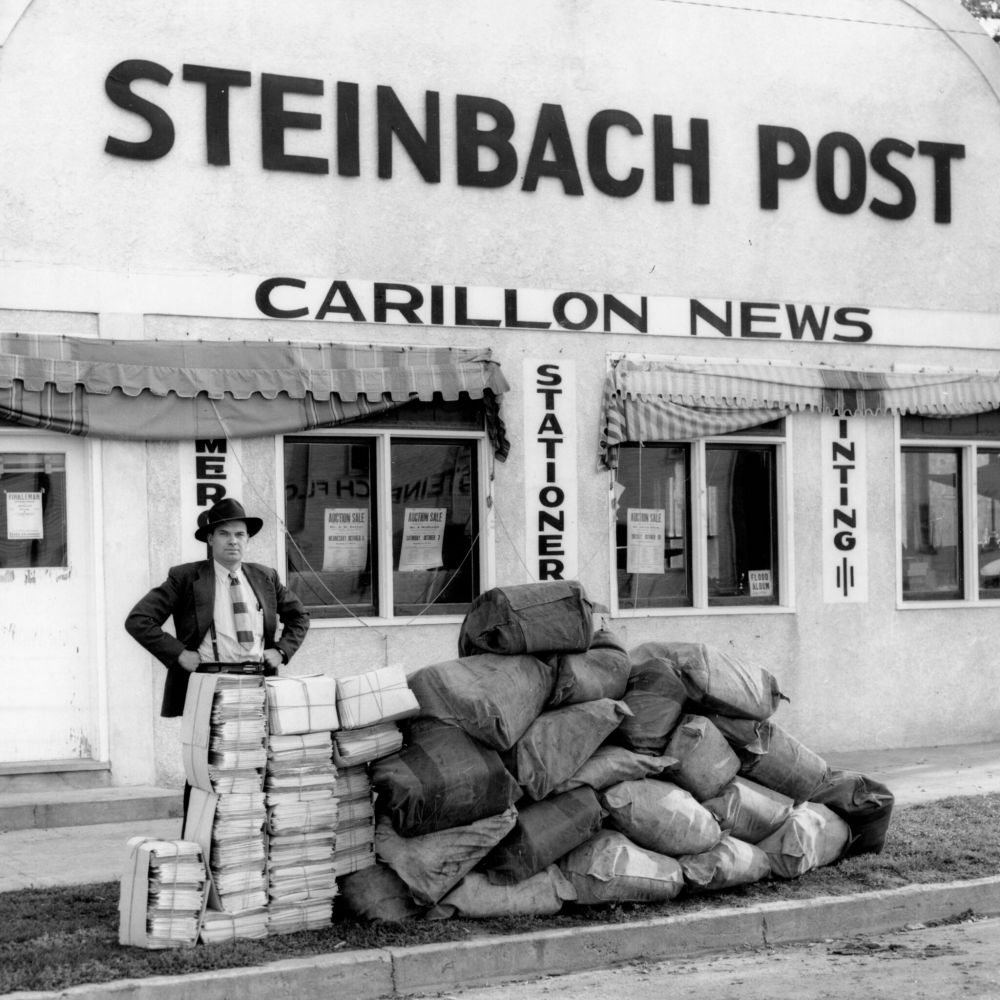 Carillon Archives
Eugene Derksen proudly displays the largest edition of The Carillon News to date, with a ton of a June, 1950 issue stacked on the sidewalk awaiting delivery to the post office.