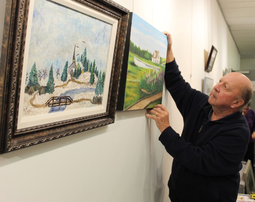 JORDAN ROSS | THE CARILLON
Gary Holden, founder of South East Artists, hangs two of his works, “Country Church” (1958) and “Prince Edward Island” (2019), in the gallery at the Steinbach Cultural Arts Centre on Tuesday.