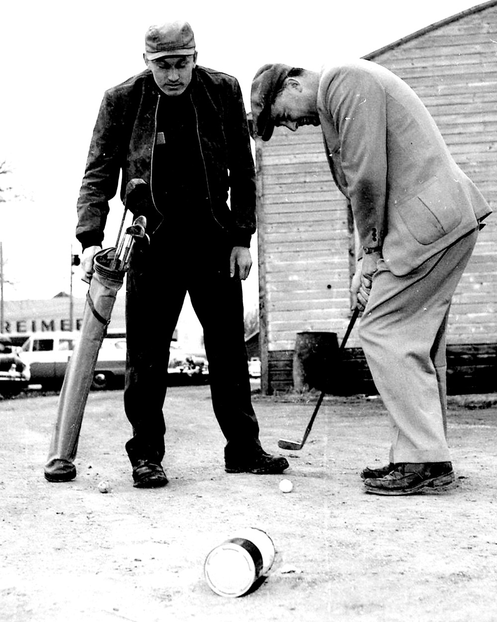 Don Toews watches as Steinbach Golf Club president Ed Regehr practices putting between customers at his garage in April of 1957. The surface of the driveway behind Regehr Garage on Main Street was similar to the sand putting surfaces at the nine-hole Steinbach golf course.
