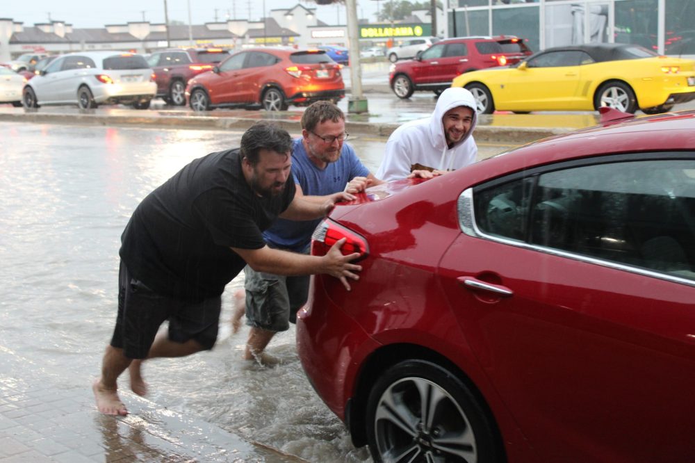 GREG VANDERMEULEN THE CARILLON
These trio of good Samaritans had no problem stepping into the driving rain, removing their footware and helping out a friend in need. This car was one of many that stalled out in the deep water present on Main Street near Brandt Street on Tuesday afternoon.