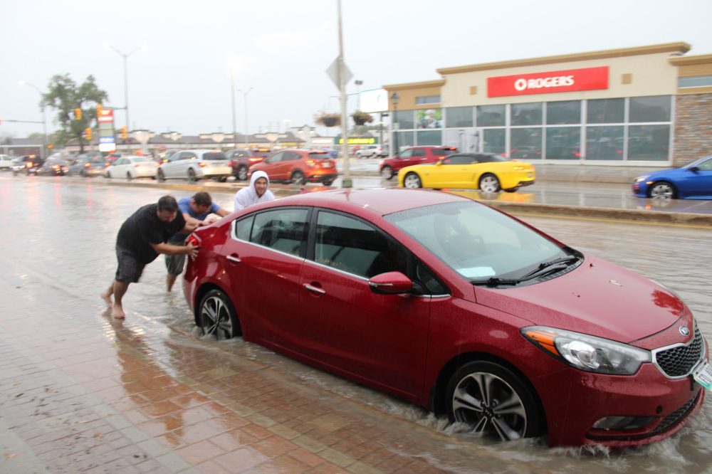 GREG VANDERMEULEN THE CARILLON
These trio of good Samaritans had no problem stepping into the driving rain, removing their footware and helping out a friend in need. This car was one of many that stalled out in the deep water present on Main Street near Brandt Street on Tuesday afternoon.