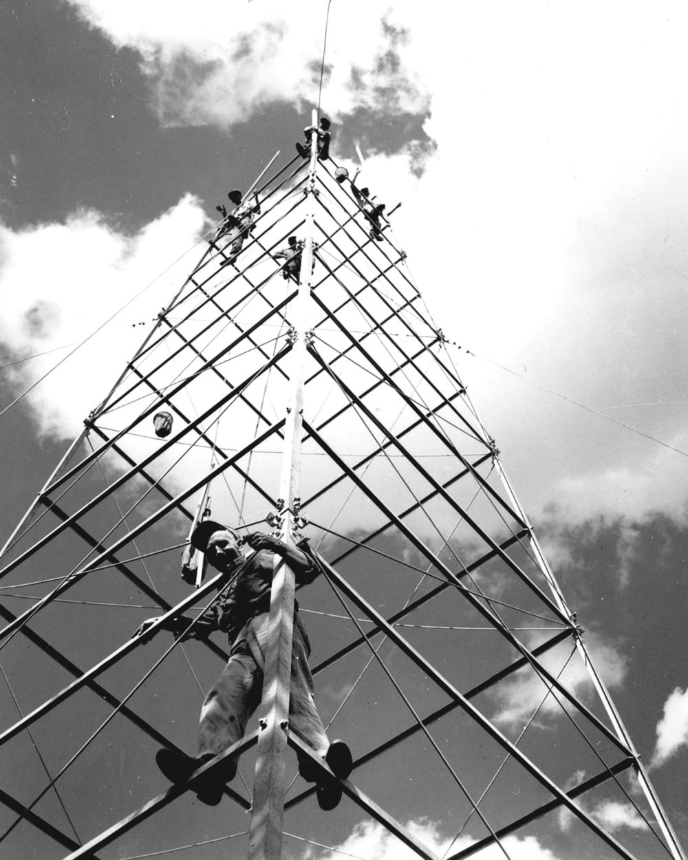 CARILLON ARCHIVES
Forest Ranger Dick Hill leaves his shady spot on the ground, climbing part way up the Bedford tower, to pose for a Carillon News photo, while high above, his crew bolts in place another section of the 80-foot lookout tower.