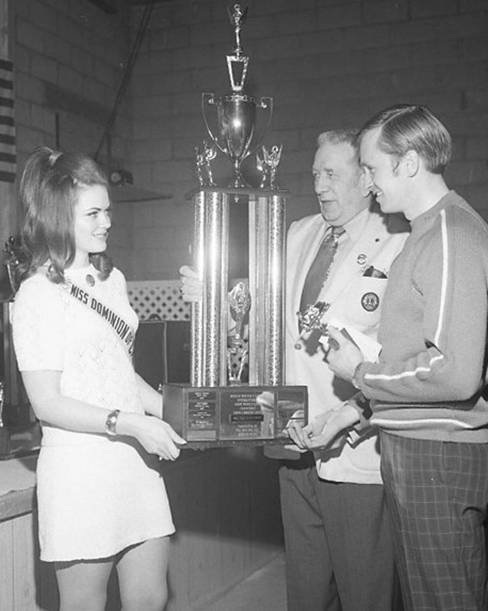 CARILLON ARCHIVES Miss Dominion of Canada, Norma Hickey, gets a little help from Roseau Lions Club president Lloyd Olson (centre) to present a trophy, nearly as tall as herself, to one of the winners at the seventh annual Roseau-Sprague International Sno-Mo-Cade.