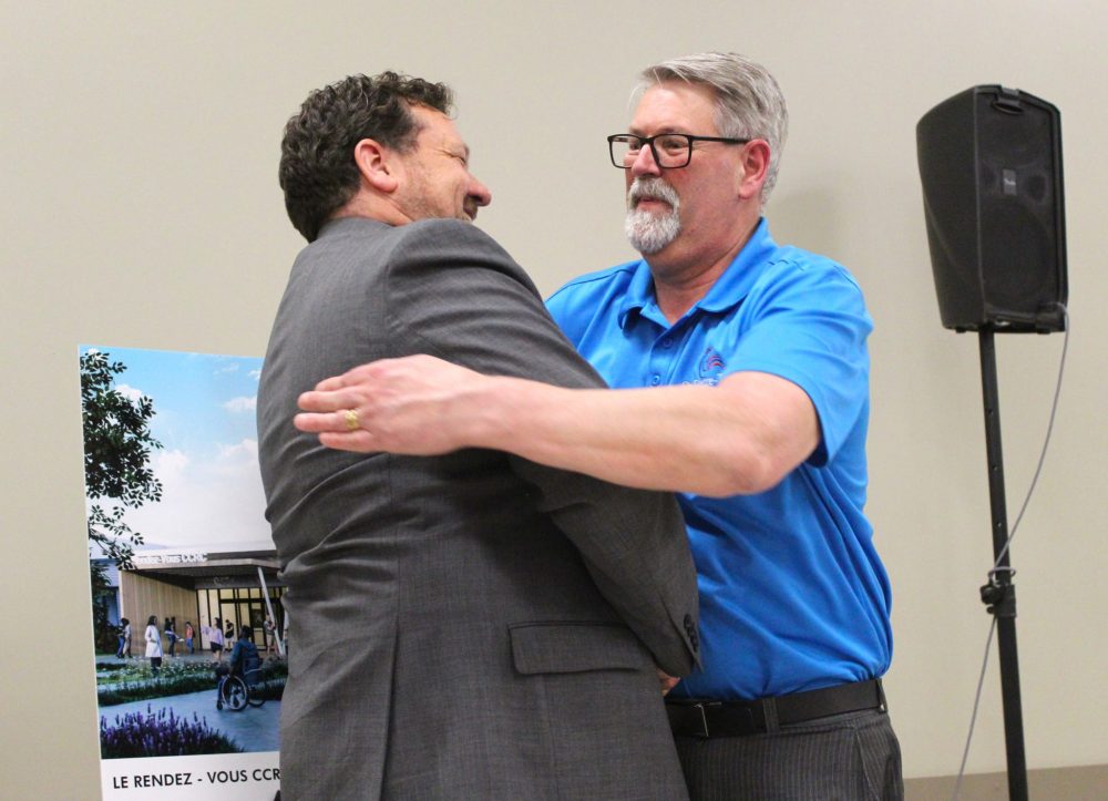 CHRIS GAREAU THE CARILLON
Minister of Municipal and Northern Relations and Minister responsible for Francophone Affairs Glen Simard (left) hugs Mayor Raymond Simard after they unveiled an illustration for the entrance of the planned Rendez-Vous community, cultural and recreational campus in St Pierre during a $5-million provincial funding announcement May 15.