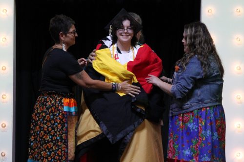 TONI DE GUZMAN THE CARILLON 

Kathryn Brisebois (middle) is wrapped with a star blanket to honour and commemorate graduating and their work with the Indigenous community.