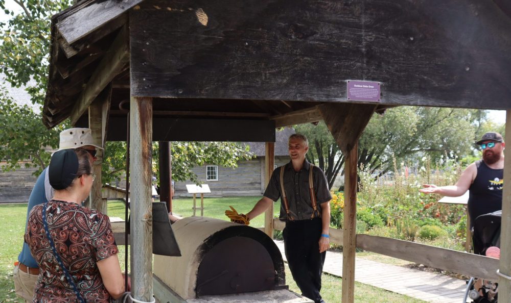 Volunteers and visitors have conversations about life in a pioneer village.