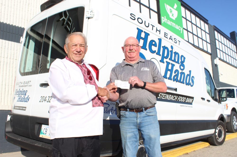 MATTHEW FRANK THE CARILLON 
Melvin Kachur hands South East Helping Hands executive director Ken Dyck a check in Steinbach on Oct. 9, 2025. Kachur pledged to donate 1,000 pounds of potatoes to the food bank.
