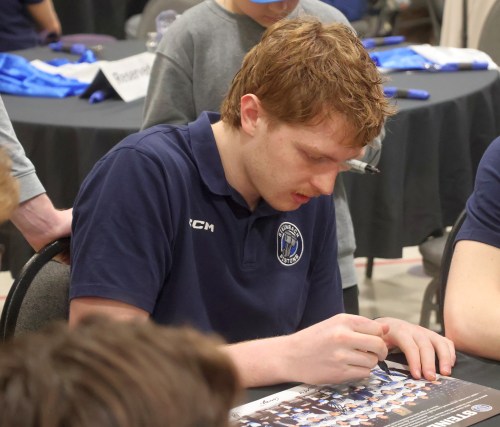 Pistons goaltender Chris Quizi signs a team photograph during the team's year-end banquet. (Cassidy Dankochik The Carillon)