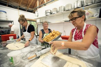 SVJETLANA MLINAREVIC THE CARILLON
Mennonite Heritage Village volunteer Trudie Kehler carries a pan full of fried rollkuchen that volunteers Beverley Sofroniuk (left) and Betty Fehr rolled and cut out during the museum's  Fall On The Farm on Sept. 7, 2026.